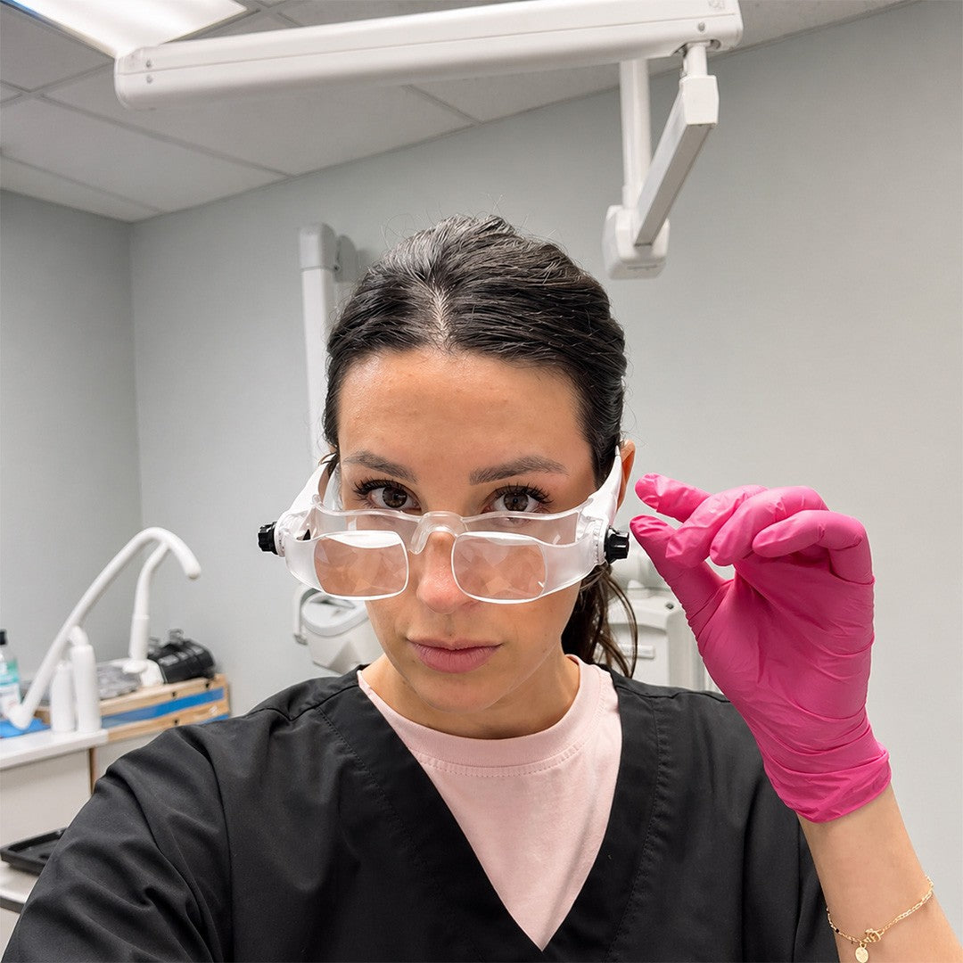 Person wearing protective eyewear and pink gloves in a dental office setting